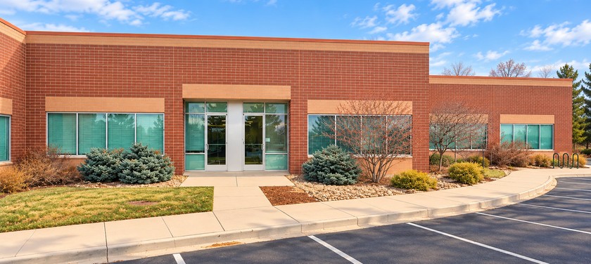 The Fake Brains office in Littleton, Colorado: a single-storey red-brick building with tinted windows and a glass entrance, under a clear blue Colorado sky.